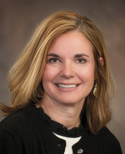 Jacinda Zerr; A woman with shoulder-length blond hair smiles warmly against a softly blurred background. She wears a black jacket and gold earrings, conveying a professional tone.