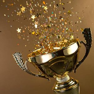 50-Year Club Awards; A gleaming gold trophy overflows with colorful confetti and star-shaped glitter, symbolizing celebration and victory against a warm brown background.