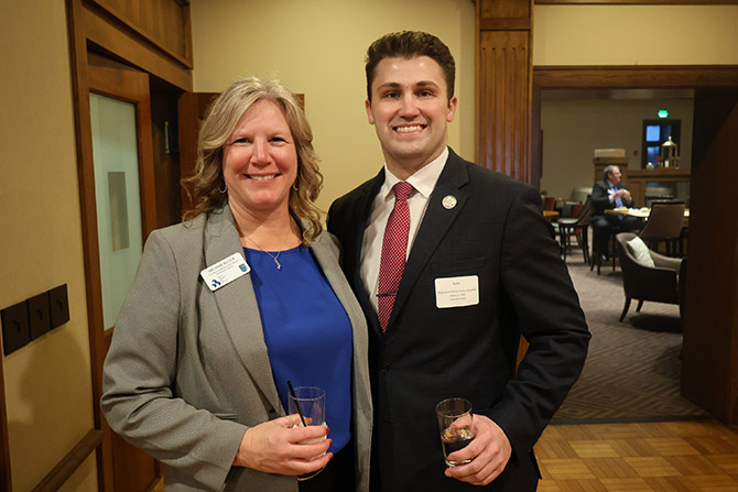 A woman and man in suites smiling holding glasses inside a building.