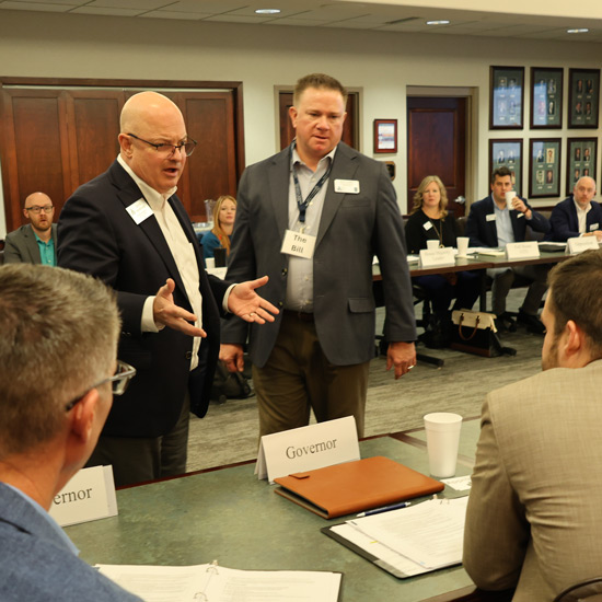 2026 Bank Leaders of Kansas Class Convenes for First Session; A man in a suit gestures while speaking to a seated group at a conference table. Attendees listen intently, with nameplates visible. The atmosphere is professional.