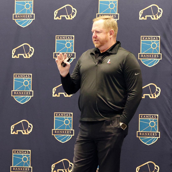2026 Bank Technology & Operations Conference Highlights; Man in black speaking with a microphone in hand, set against a Kansas Bankers backdrop with buffalo and badge logos, conveying a professional tone.