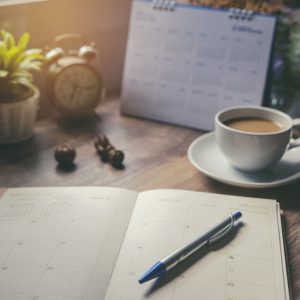 2026 KBA Calendar; Open planner with a pen, beside a coffee cup, clock, and calendar on a wooden table. Soft morning light creates a calm, focused ambiance.