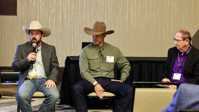 Three men sit on chairs in a panel discussion. Two wear cowboy hats and casual attire, while the third wears a suit. The setting is professional and focused.
