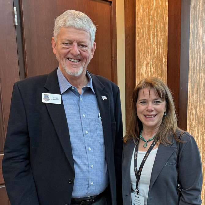A man and a women wearing professional attire smile while wearing badges at a conference.