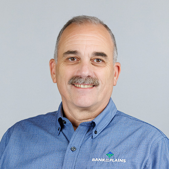 2026 Kansas Ag Bankers Pioneer Award Recipient Pat Fallon; Smiling man with a mustache in a blue "Bank of the Plains" shirt against a plain gray background, conveying a professional and approachable demeanor.