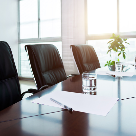 New Bankers Join Kansas State Banking Board; Modern conference room with black leather chairs around a polished table. Papers, pens, and glasses of water are arranged neatly. Sunlight filters through large windows.