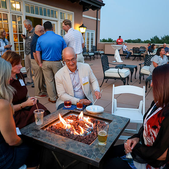 2026-CEO-&-Senior-Management-FEATURE - people sitting around an artificial fire pit roasting marshmallows and drinking refreshments.