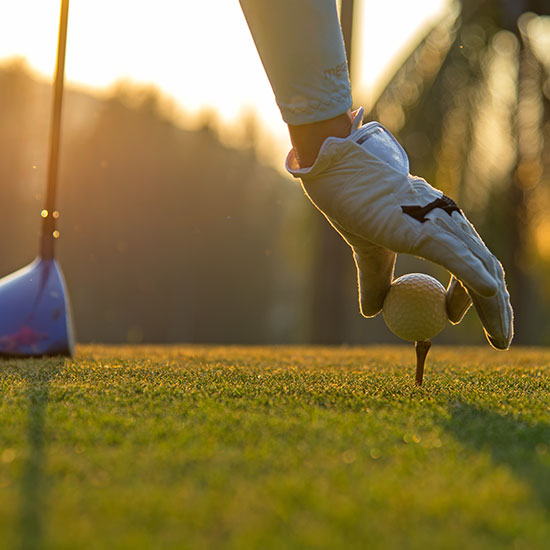 Man placing a ball onto a golf tee with a blurred out sunset in the background. Picture taken close to the ground at the ball's level